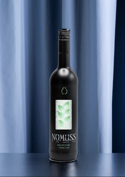 Zwarte fles Nomuss Mojito Mix (0,75L) met groen bladmotief op het etiket, gefotografeerd tegen een donkerblauwe gordijnachtergrond. Op de fles staat 'No Fuss Cocktail Mixers' en '15 serves'.